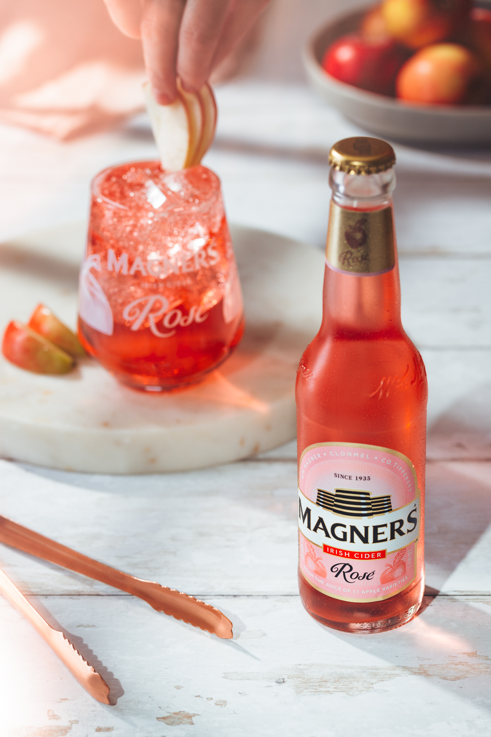 Magners Rose cider bottle on white wooden table with apples