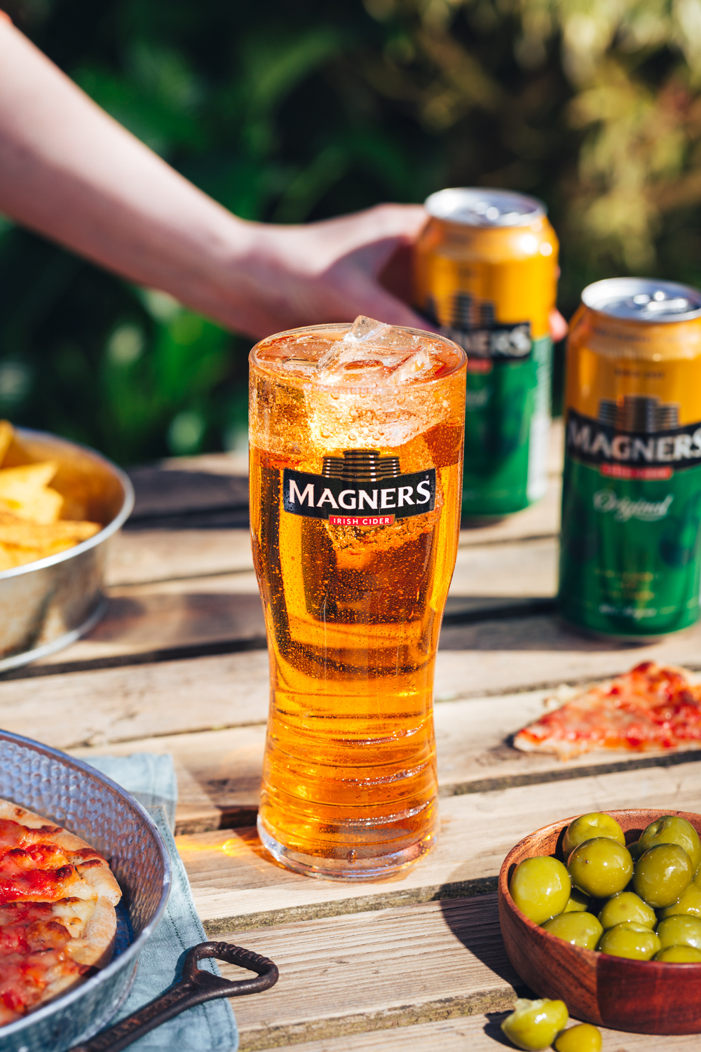 Magners cider bottle on picnic table with a hand in the background