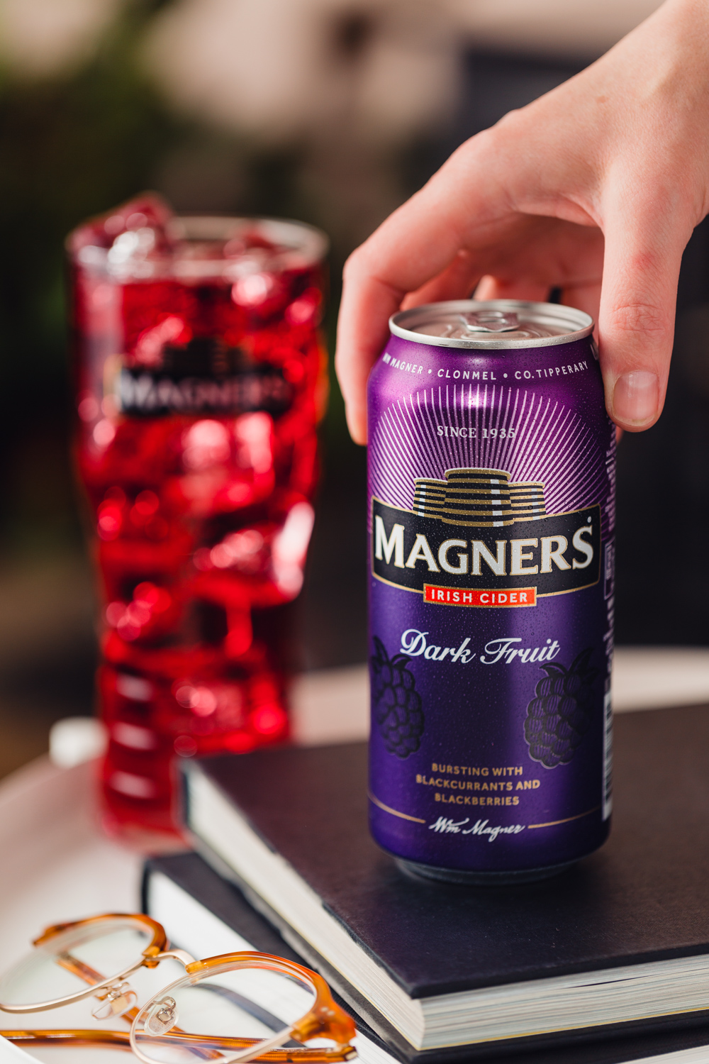 Magners Dark Fruit can on a book with a handing grabbing it