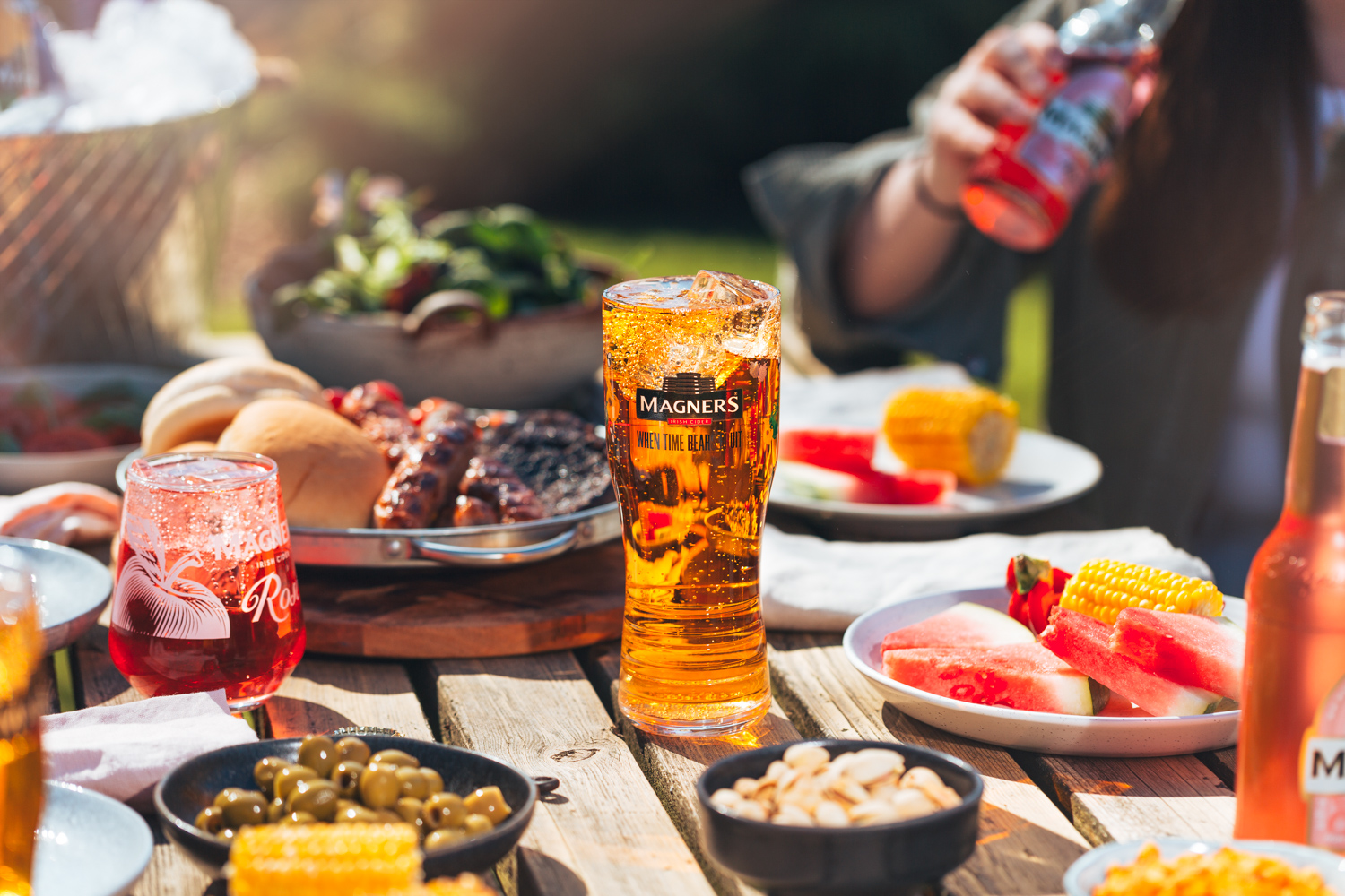 Glass of Magners cider on a picnic table with BBQ food