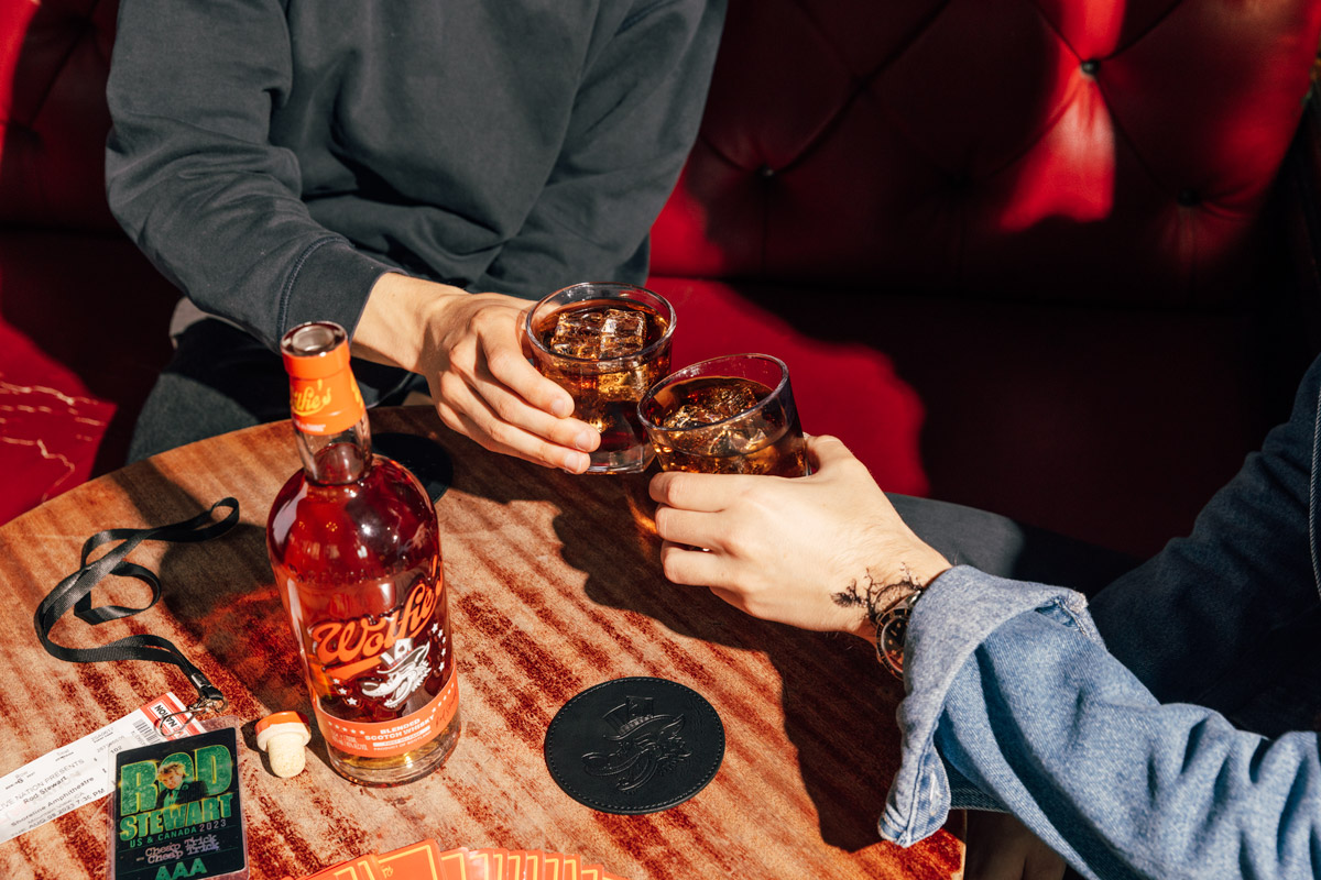 Two people doing a cheers of whisky and coke at a bar table