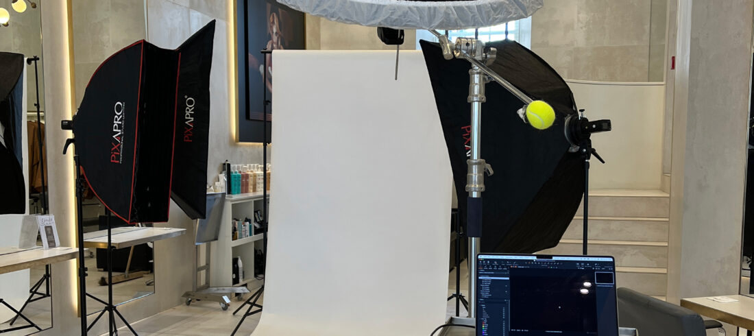 headshot photography edinburgh BTS Behind-the-scenes setup of a headshot photography session in an Edinburgh salon, showing a white paper backdrop with two Pixapro softboxes, a large overhead beauty dish on a boom arm with a tennis ball counterweight, a tethered MacBook running Capture One, and a remote trigger on the backdrop.